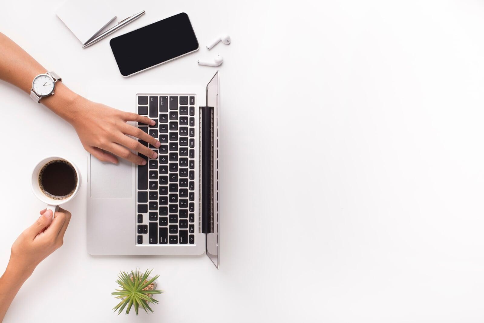 Top-down view of a tidy white desk with a laptop, coffee, and accessories, showing effective desktop organization ideas.