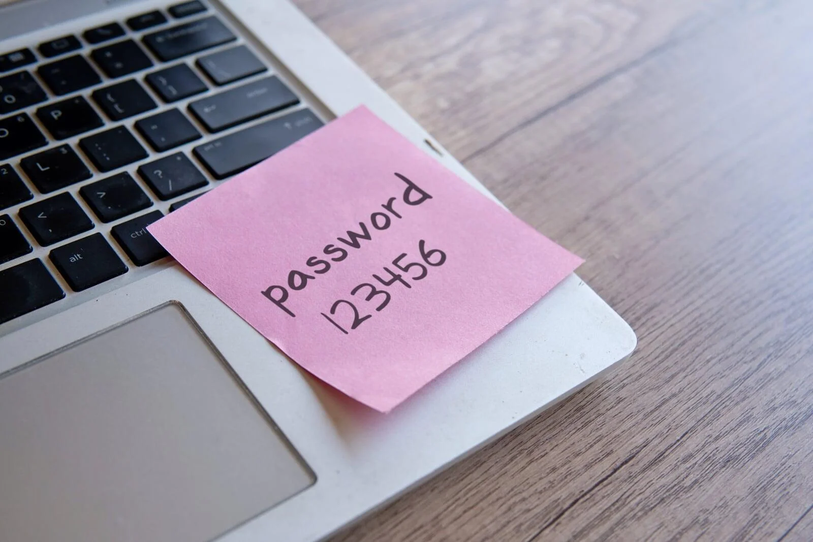 Hand hovering over a laptop with red and blue lock icons, illustrating how one password can compromise multiple accounts in a password spraying attack.