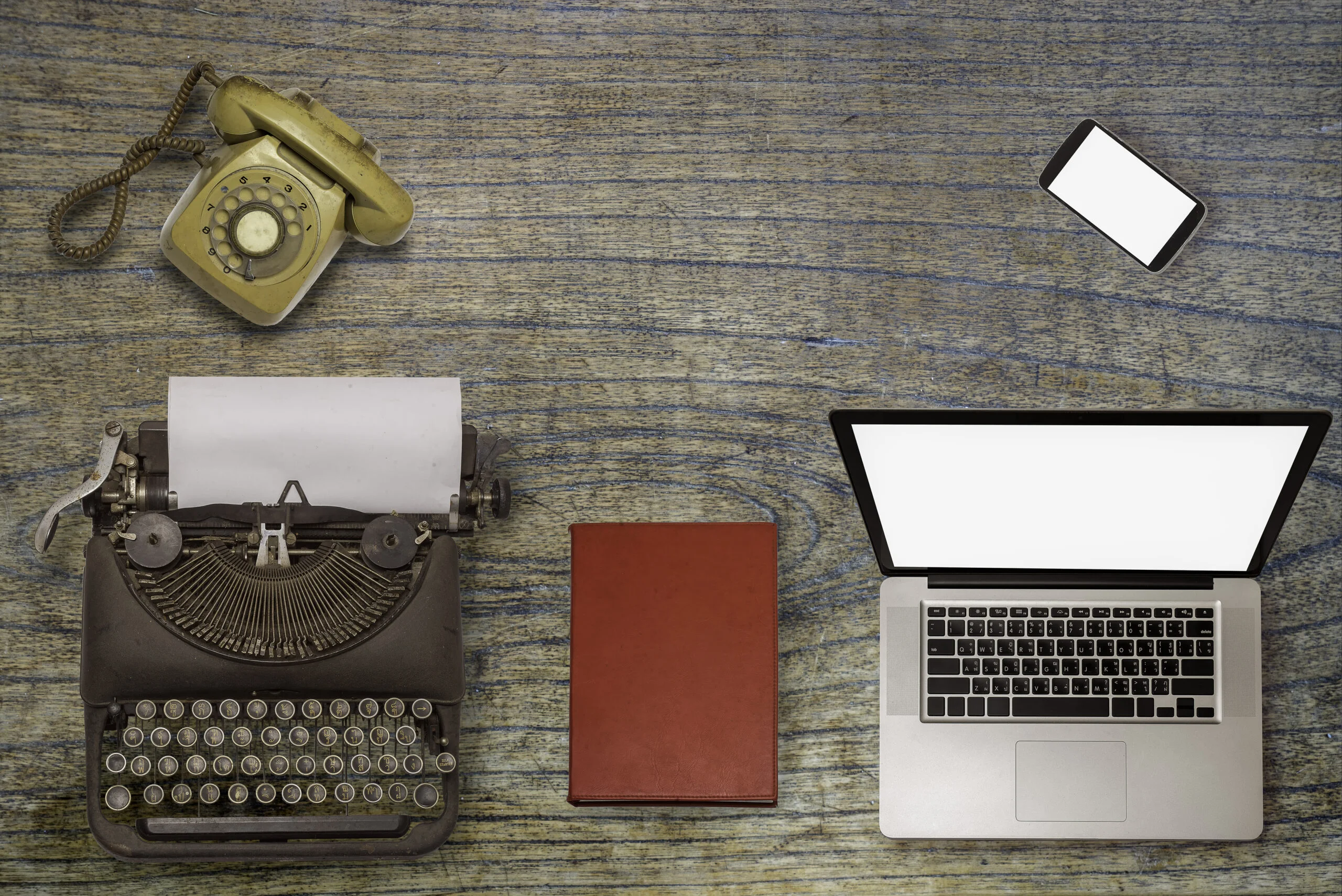 A typewriter and rotary phone next to a modern laptop and smartphone, illustrating the necessity of an IT refresh plan for small businesses to replace legacy hardware.