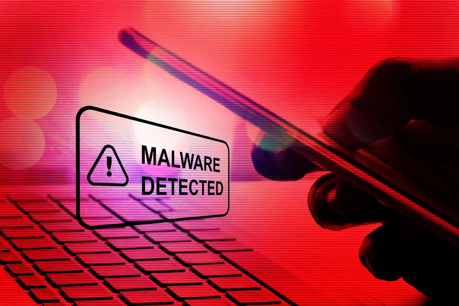 A smartphone showing a red “Malware Detected” alert over a keyboard, symbolizing a security breach caused by malvertising attacks.