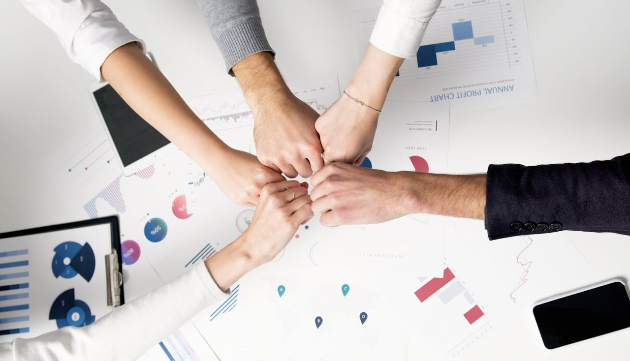 Overhead view of five people doing a fist bump over business charts, symbolizing teamwork and great digital employee experience.