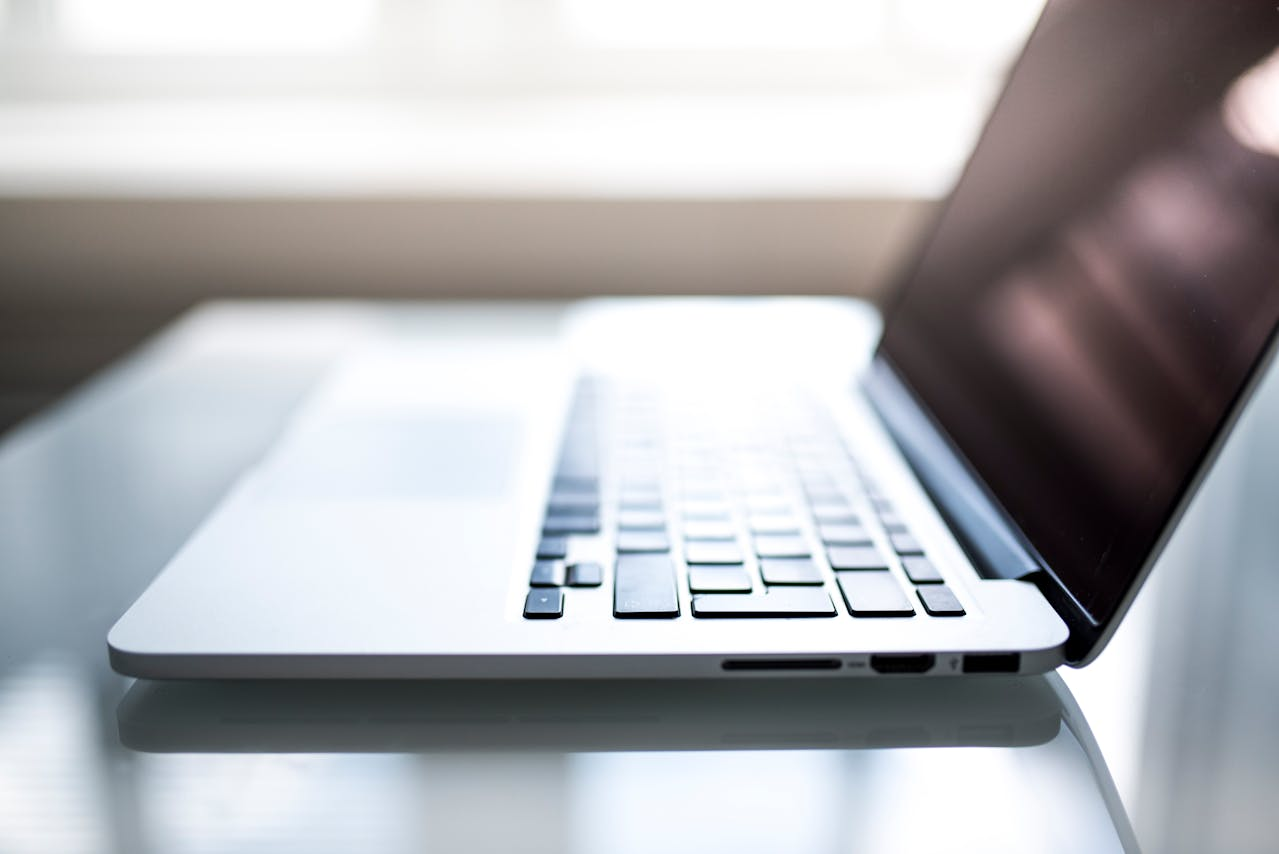 Side view of an open silver laptop on a glass desk, symbolizing IT compliance best practices in a work environment.
