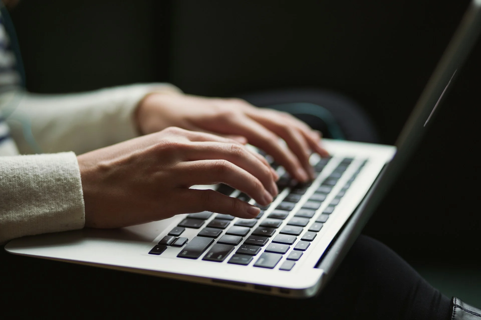 A close-up side view of a person's hands typing on a laptop keyboard against a dark background, illustrating an IT administrator executing identity governance policies and revoking admin rights on a local endpoint.