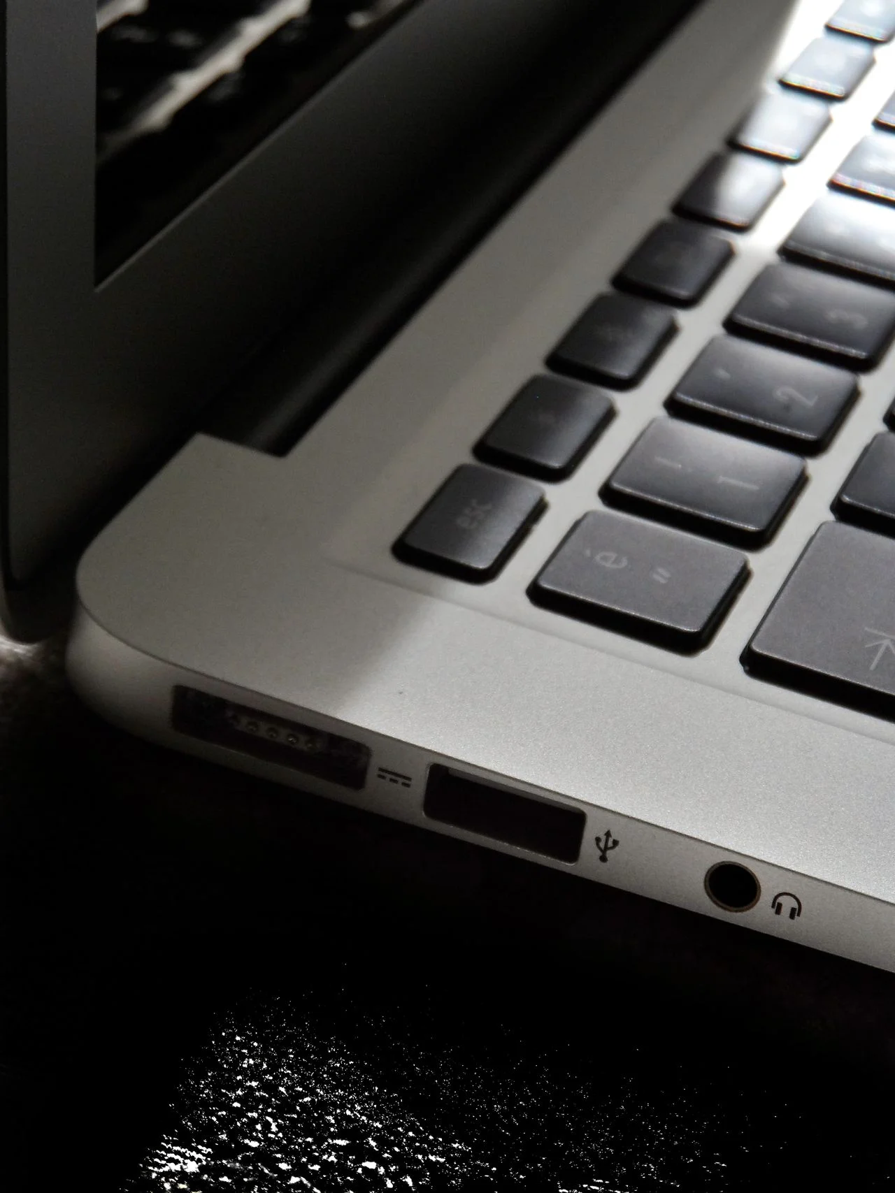 A vertical, close-up shot of a silver laptop keyboard and its side connectivity ports, representing an open workstation being checked during a SaaS offboarding security audit.