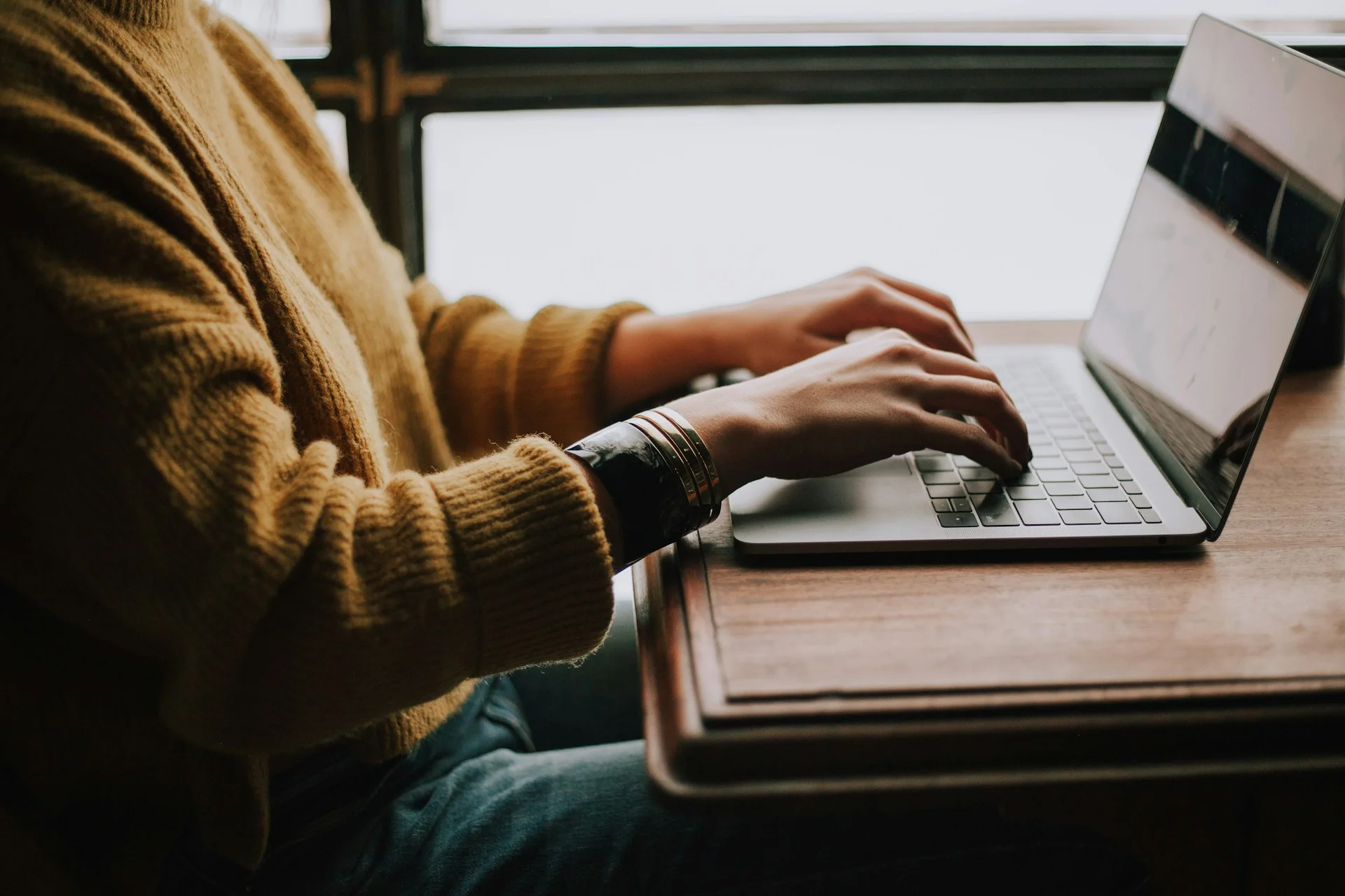 Professional typing on a laptop keyboard at a wooden desk, illustrating passwordless login and Passkeys for business.