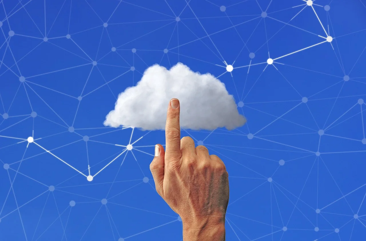 A hand pointing toward a cloud against a blue background with interconnected network lines, representing cloud storage and collaboration for OneDrive vs SharePoint.